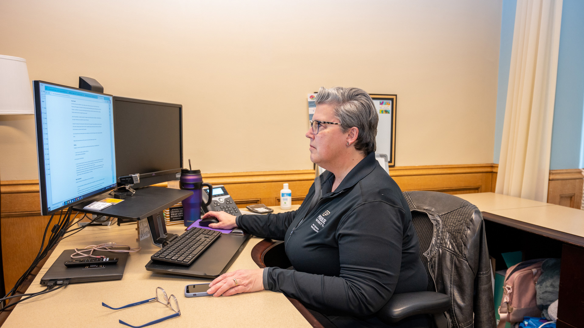 A professional is seated at a desk in front of a computer screen, focused on the content displayed, in an office environment.